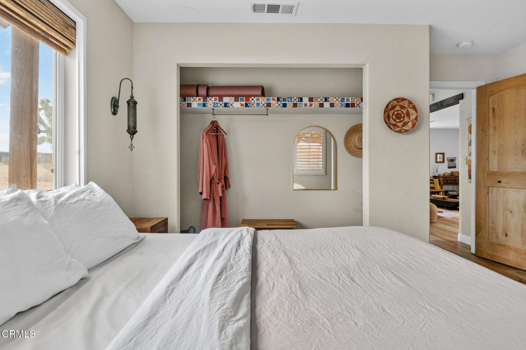 Bedroom with a white bed, recessed closet, coral robe, and window with a wooden shade.