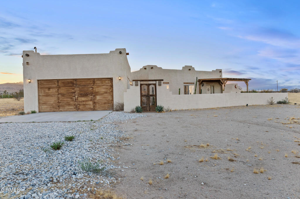 Desert home with white stucco walls, a wooden garage door, and a covered porch.