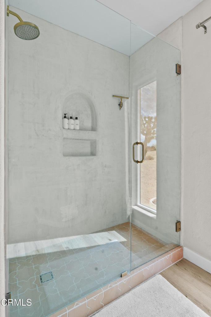 Walk-in shower with glass enclosure, brass fixtures, recessed shelves, and patterned tile floor.