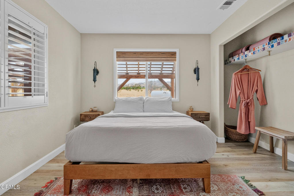 Furnished bedroom with a wooden bed, shuttered windows, and a walk-in closet with a hanging robe.