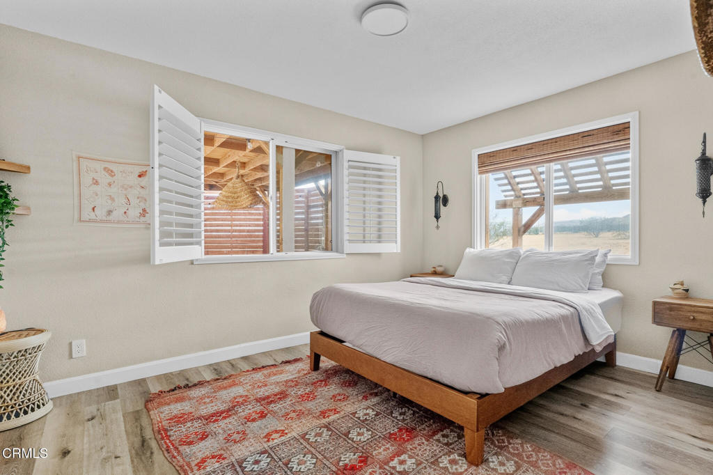 Bedroom with white bedding, a patterned rug, and shuttered windows overlooking a covered patio.