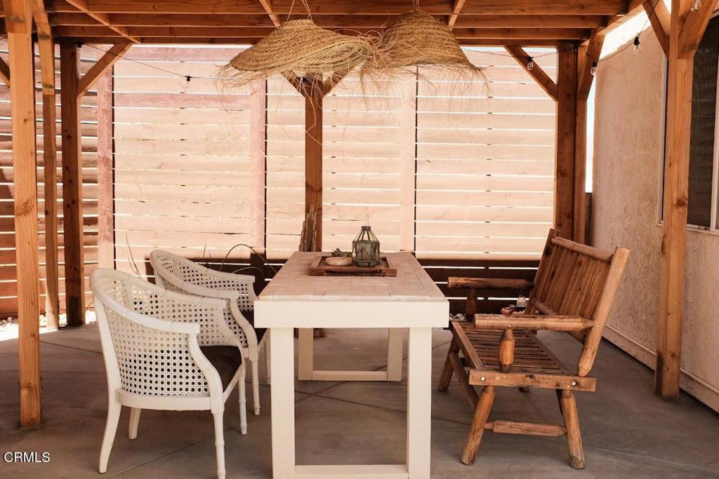 Covered patio with a dining table, woven chairs, wooden bench, and slatted privacy screens.