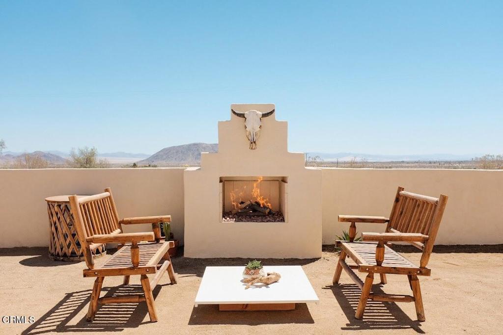 Outdoor patio with a built-in fireplace, wooden chairs, and distant desert mountains.