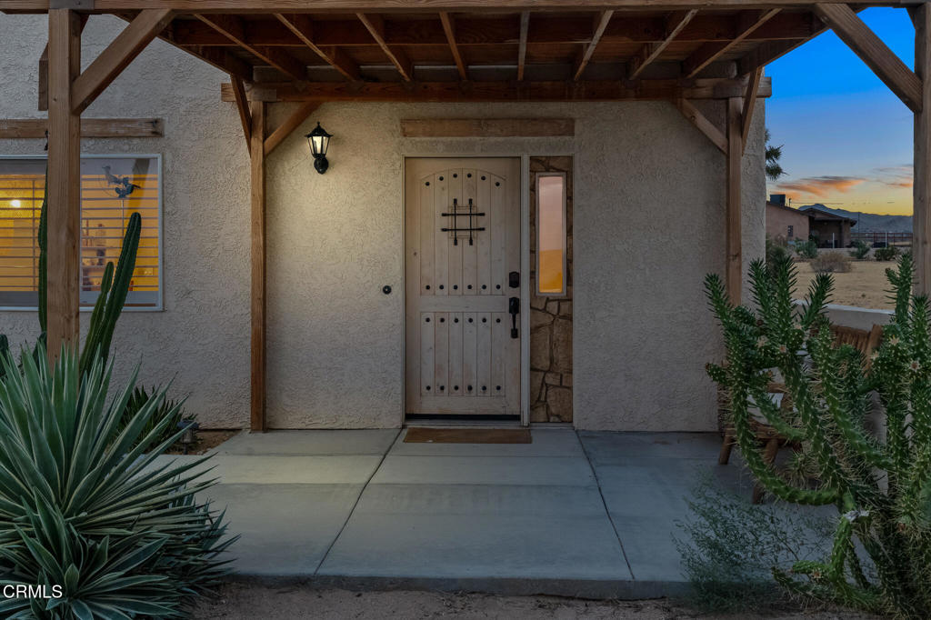 Home entrance beneath a timber porch, with a paneled door and desert landscaping.
