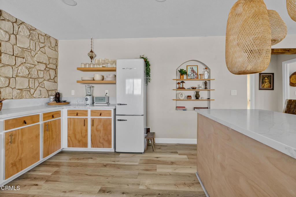 Kitchen with natural wood cabinets, a stone accent wall, and a large white-countertop island.