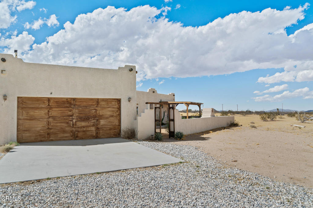 Stucco home with a wooden garage door and gravel driveway in a desert setting.