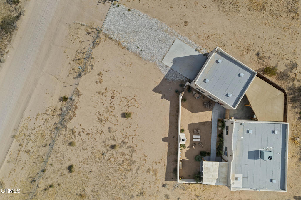 Aerial view of two flat-roofed buildings and a walled patio on a sandy desert lot.