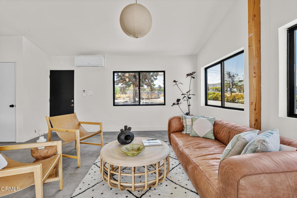 Living room with a brown leather sofa, wooden lounge chairs, and large windows overlooking the desert.