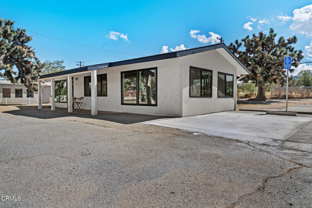 White stucco building with dark trim, large windows, a covered porch, and paved parking.