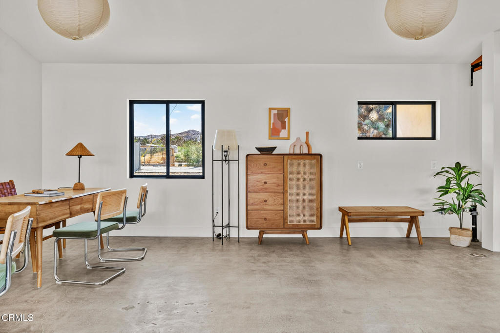 Staged dining room with a cane-front sideboard, wooden table, and windows overlooking desert hills.