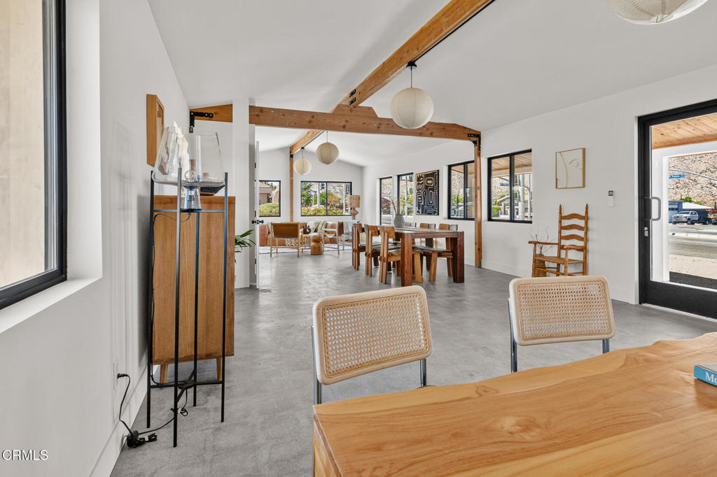 Open-plan dining area with a long wooden table, exposed beams, and concrete floors.