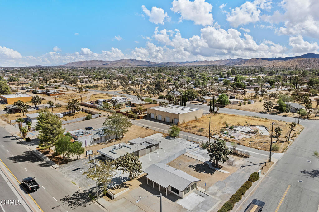 Aerial view of a low commercial building and paved lot, with desert mountains on the horizon.