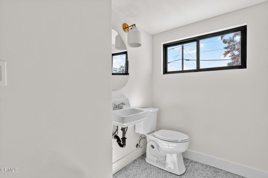 Bathroom with a pedestal sink, toilet, high black-framed window, and hexagonal mosaic tile floor.
