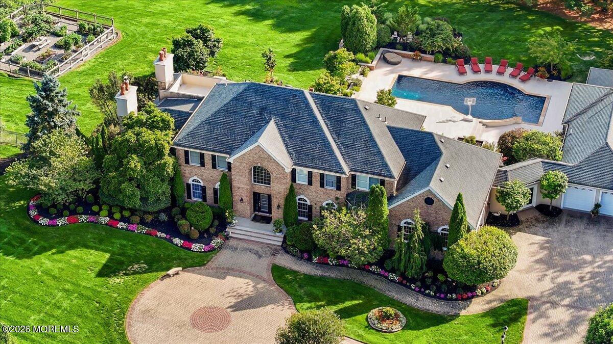 Aerial view of a brick home with a circular driveway, landscaped grounds, and backyard pool.