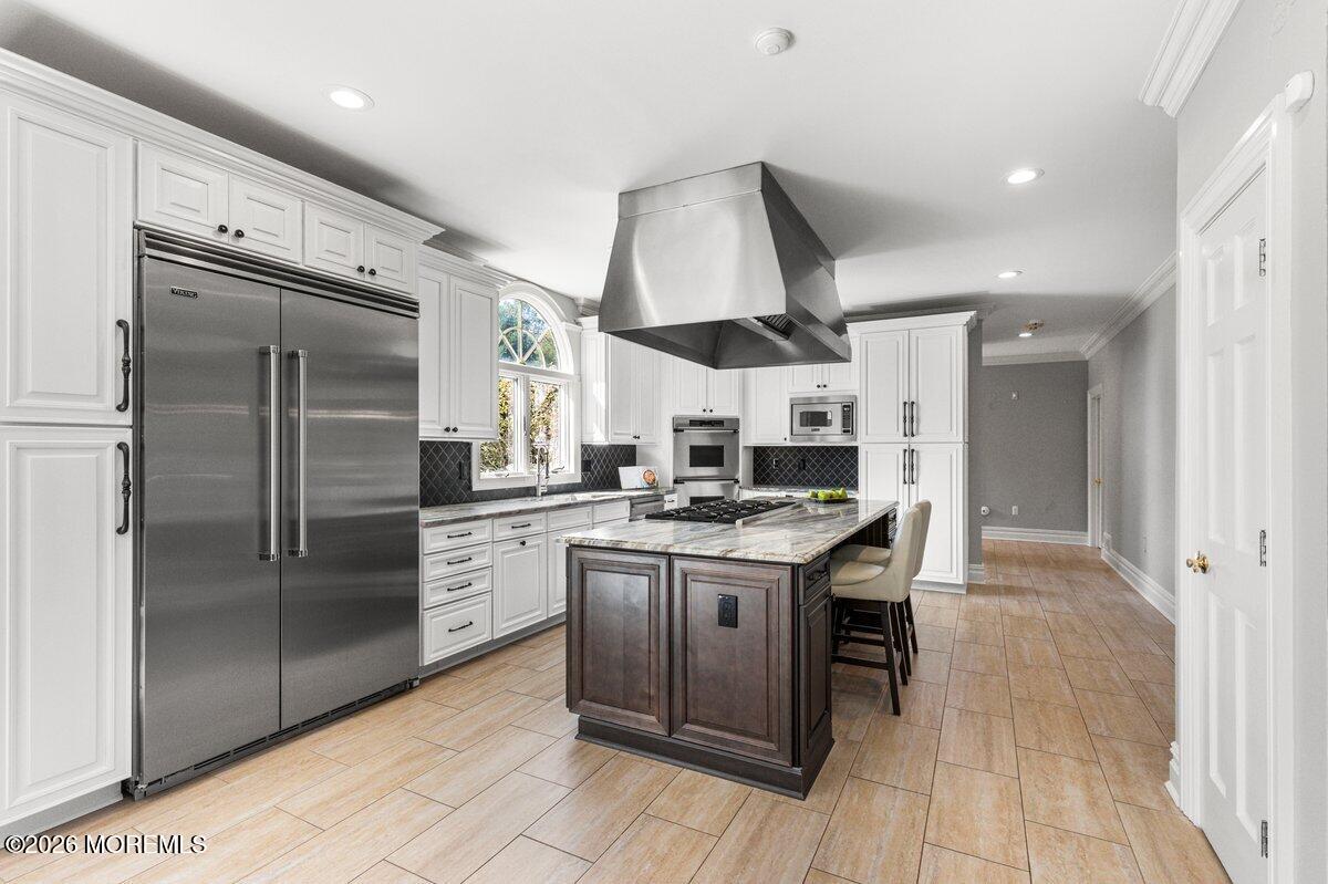 Kitchen with a dark wood island, marble countertop, stainless range hood, and white cabinets.