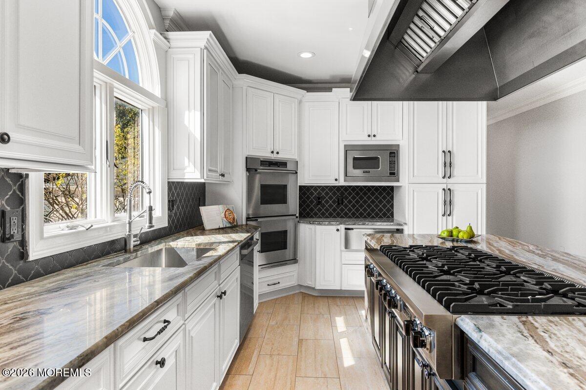Kitchen with white cabinetry, marble counters, a large gas range, and an arched window over the sink.