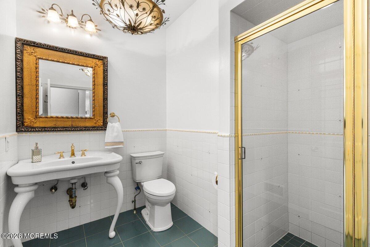 Bathroom with a pedestal sink, ornate gold-framed mirror, and glass shower with gold-colored trim.