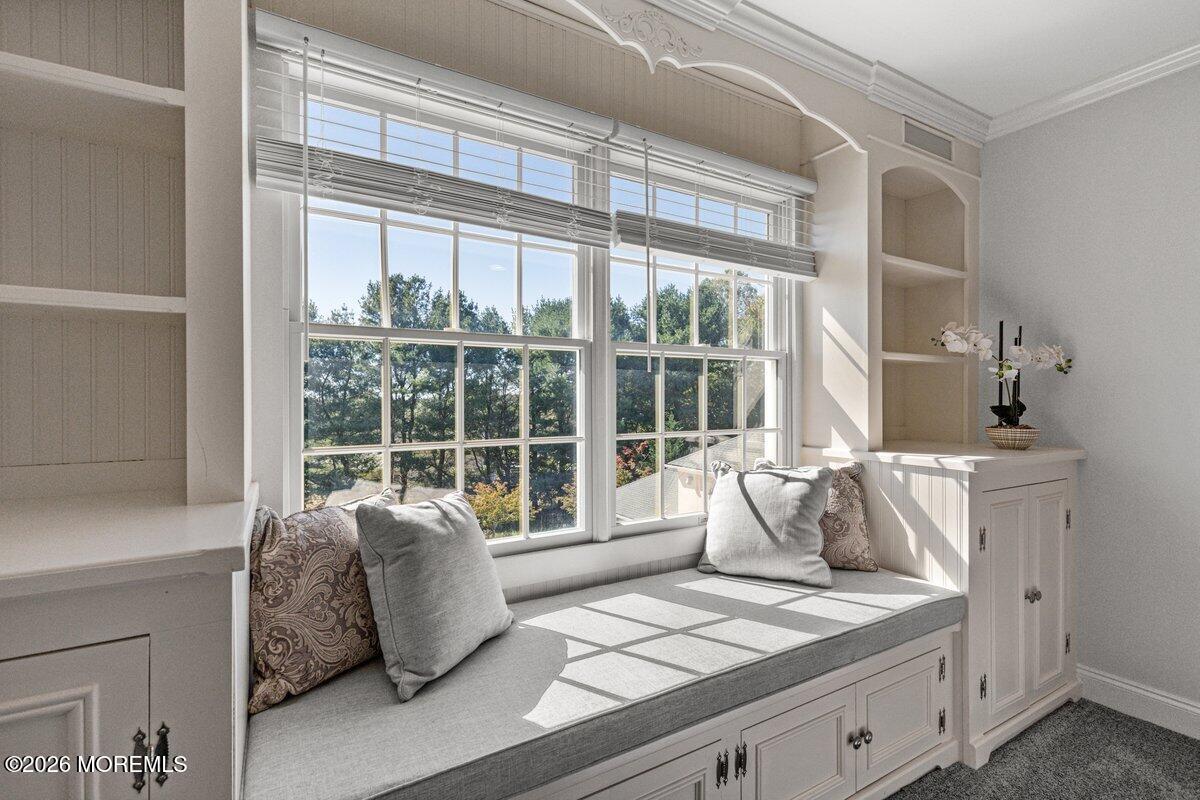 Built-in window seat with gray cushions beneath large windows overlooking trees.