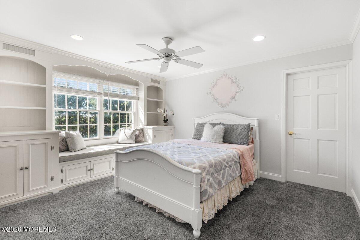 Bright bedroom with a white bed and built-in window seat beneath large multi-pane windows.
