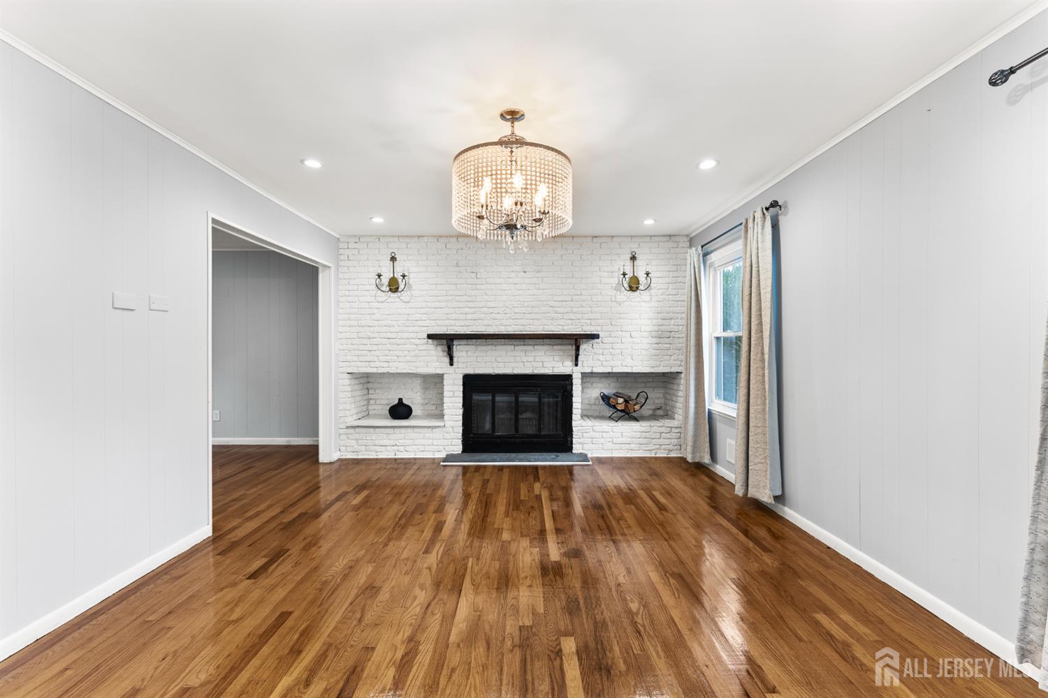 Living room with a white brick fireplace, polished hardwood floors, and a crystal chandelier.