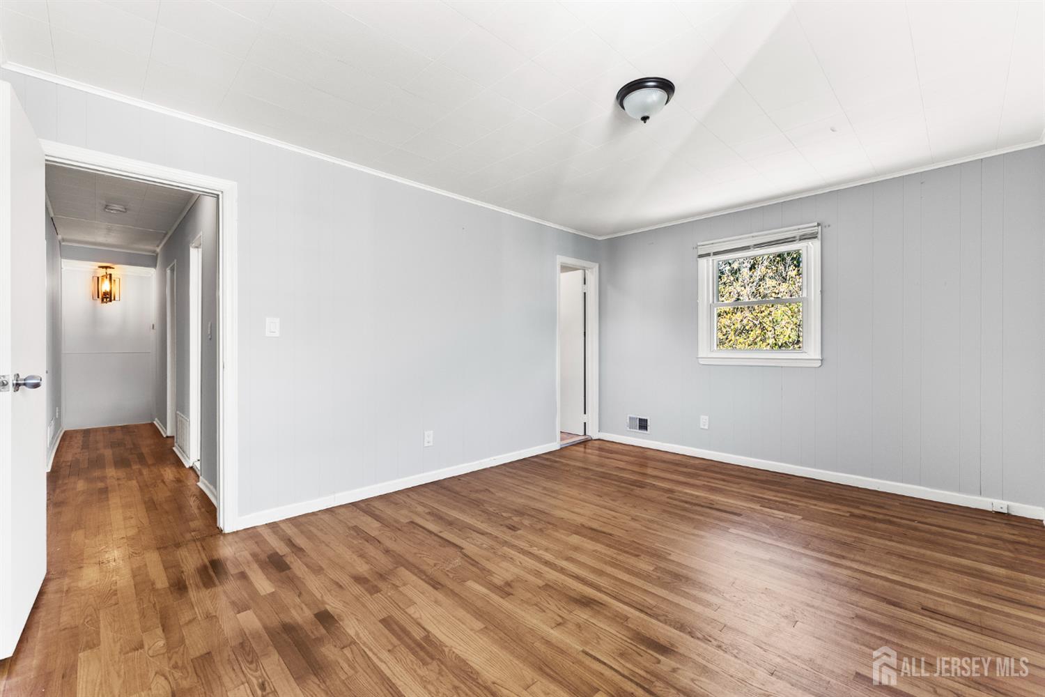 Empty room with gray walls, hardwood floors, and a window overlooking trees.