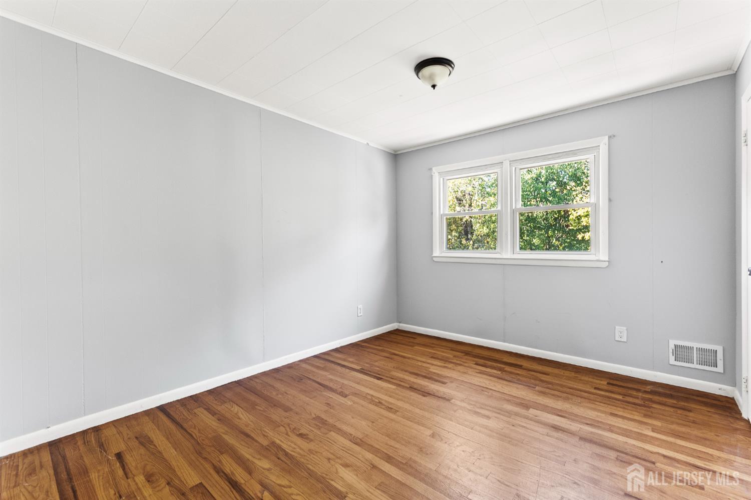 Empty room with hardwood floors, gray walls, and a double window.