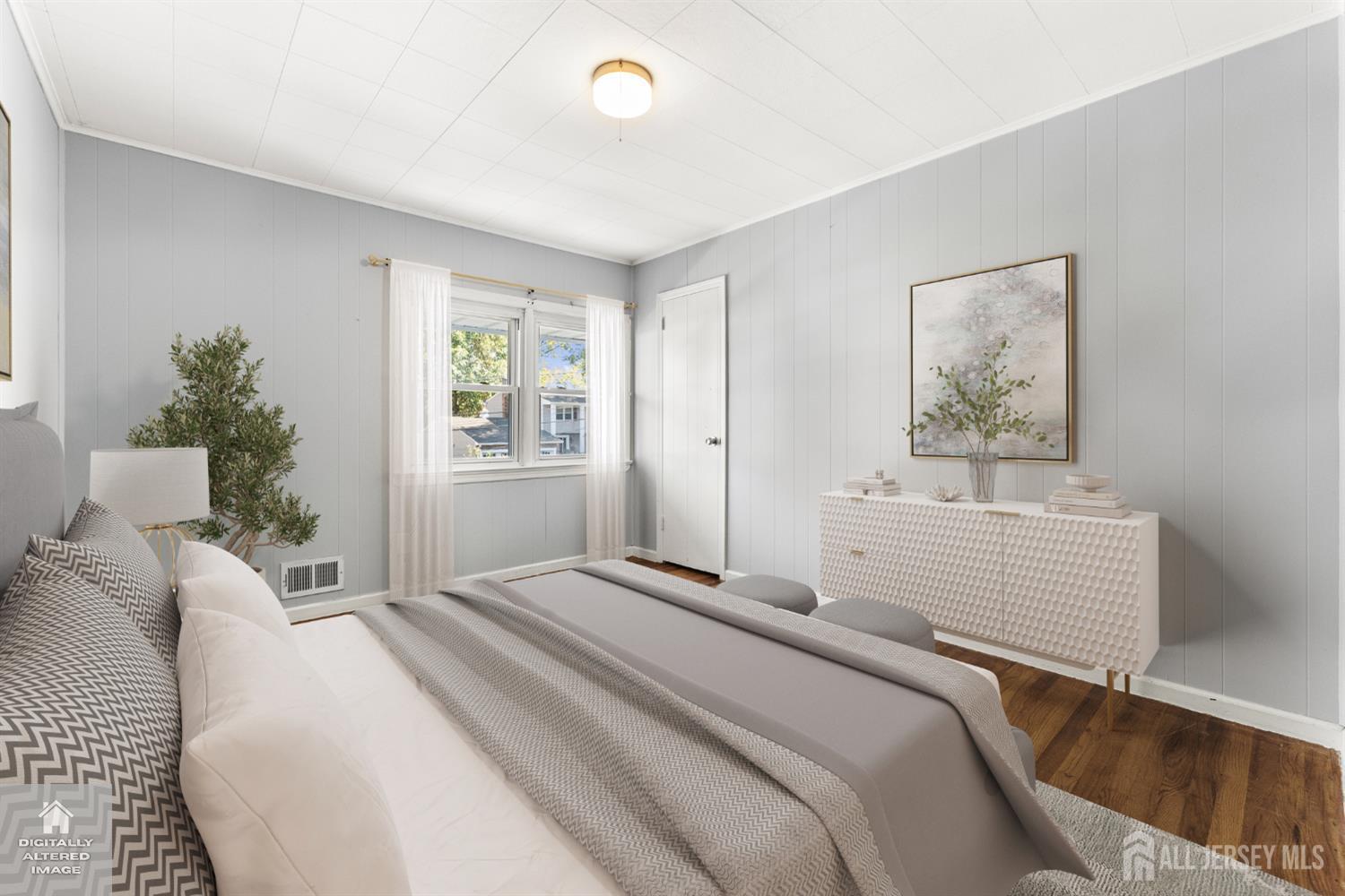 Staged bedroom with gray and white bedding, paneled walls, and a white textured dresser.
