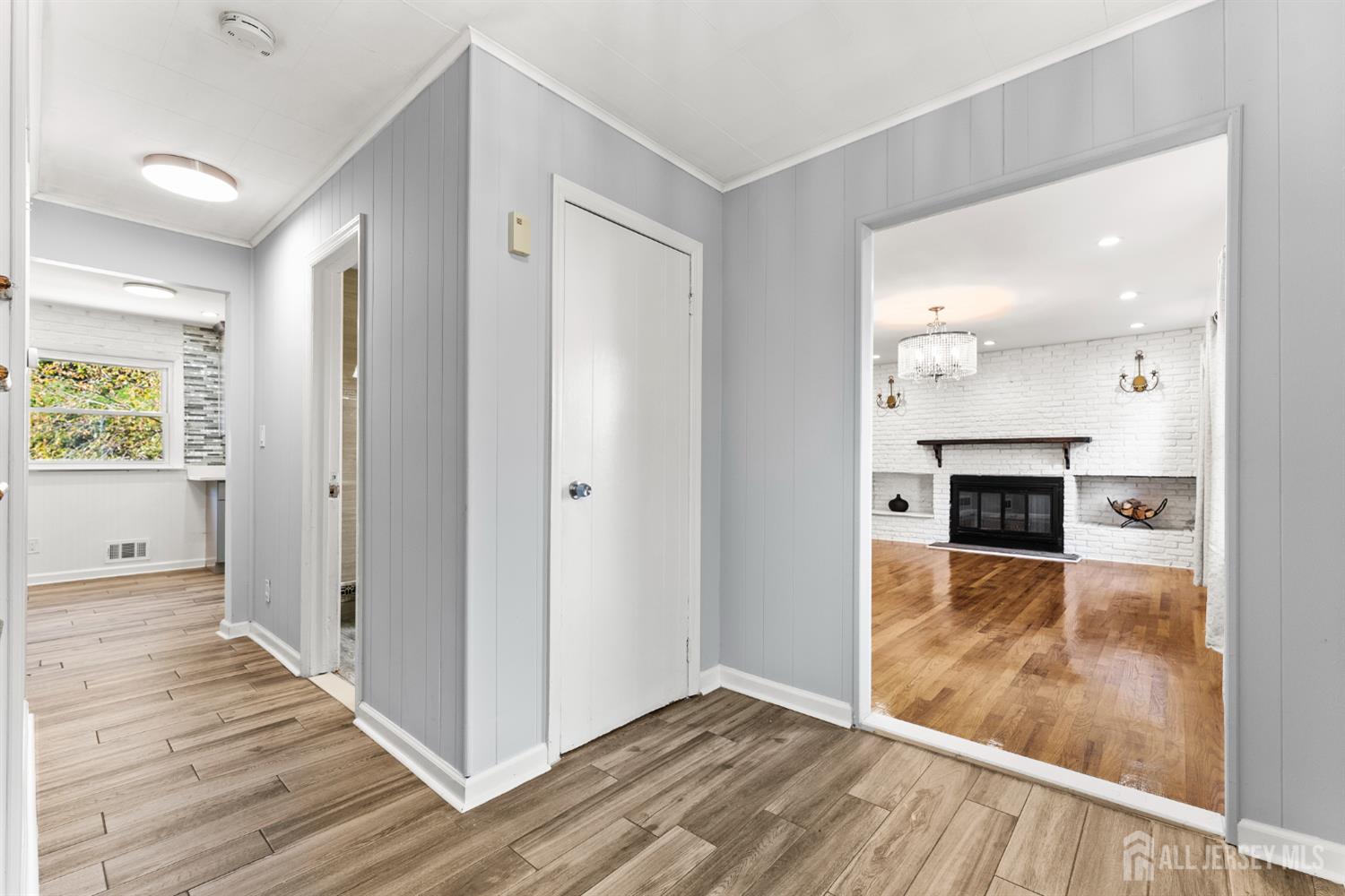 Gray paneled hallway opening to a living room with a white brick fireplace and hardwood floors.