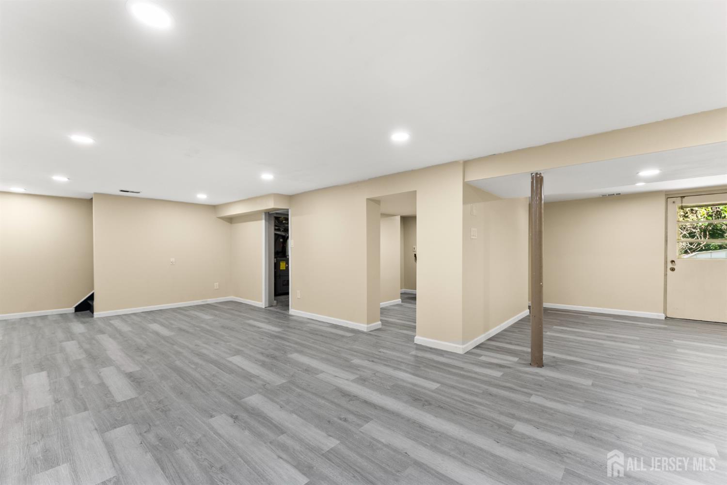 Finished basement with gray plank flooring, recessed lights, and an exposed support post.