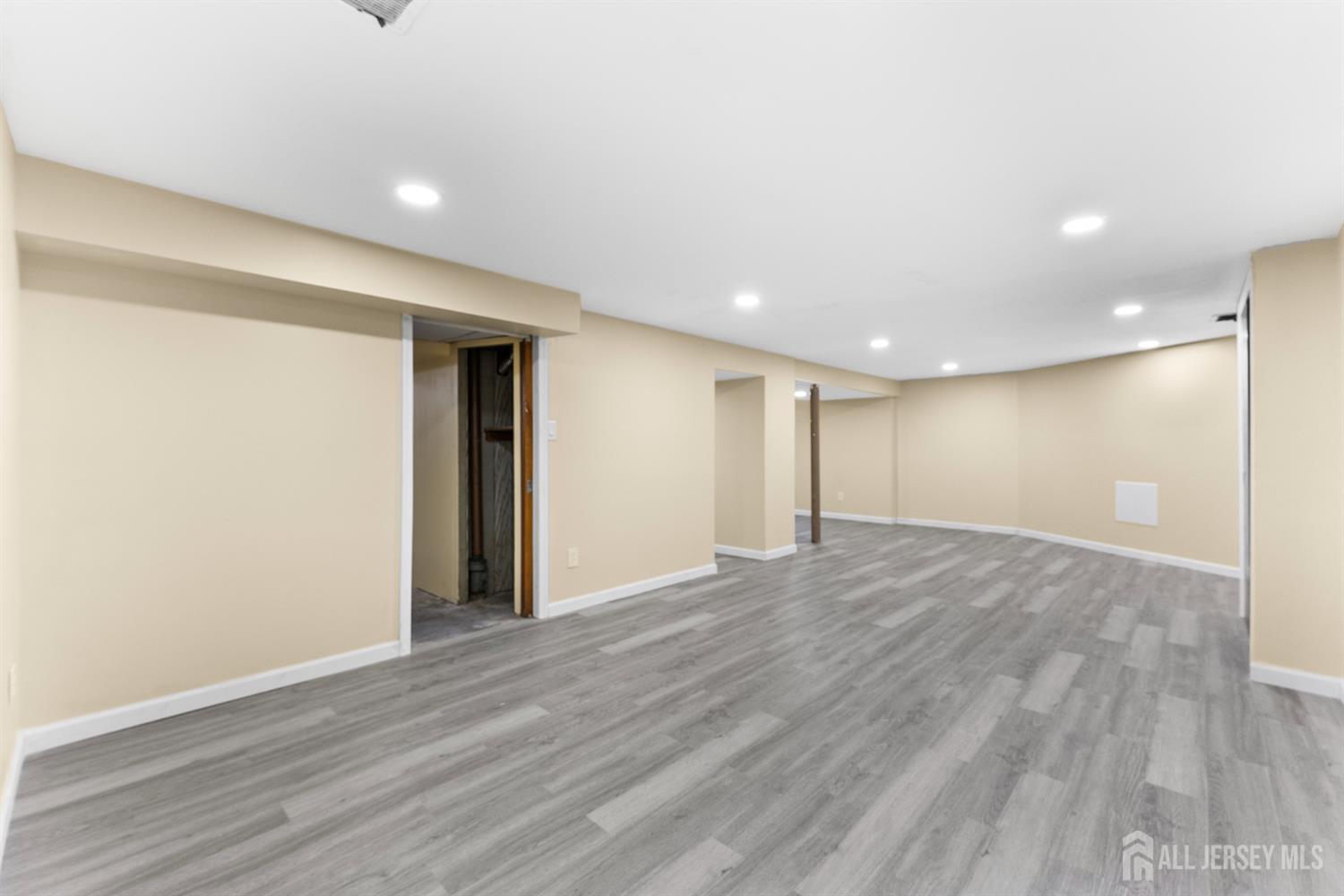 Finished basement with gray plank flooring and recessed lights.