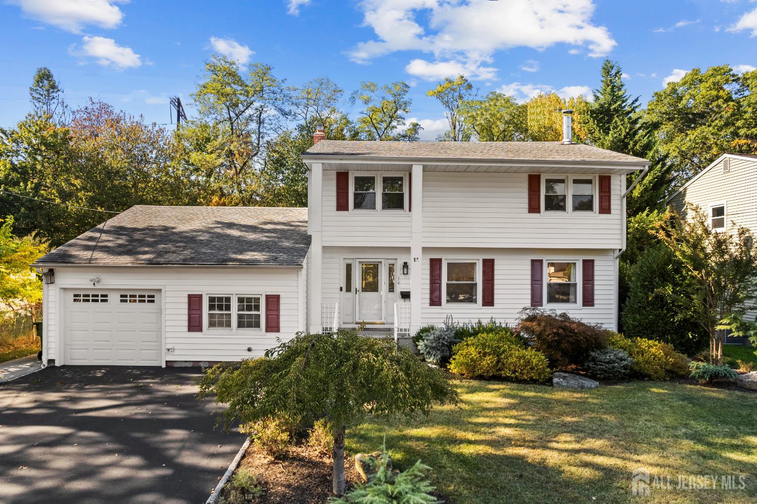 White two-story house with red shutters, attached garage, landscaped yard, and paved driveway.