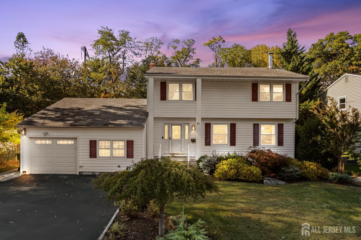 Two-story home with an attached garage, red shutters, and a landscaped front lawn at dusk.