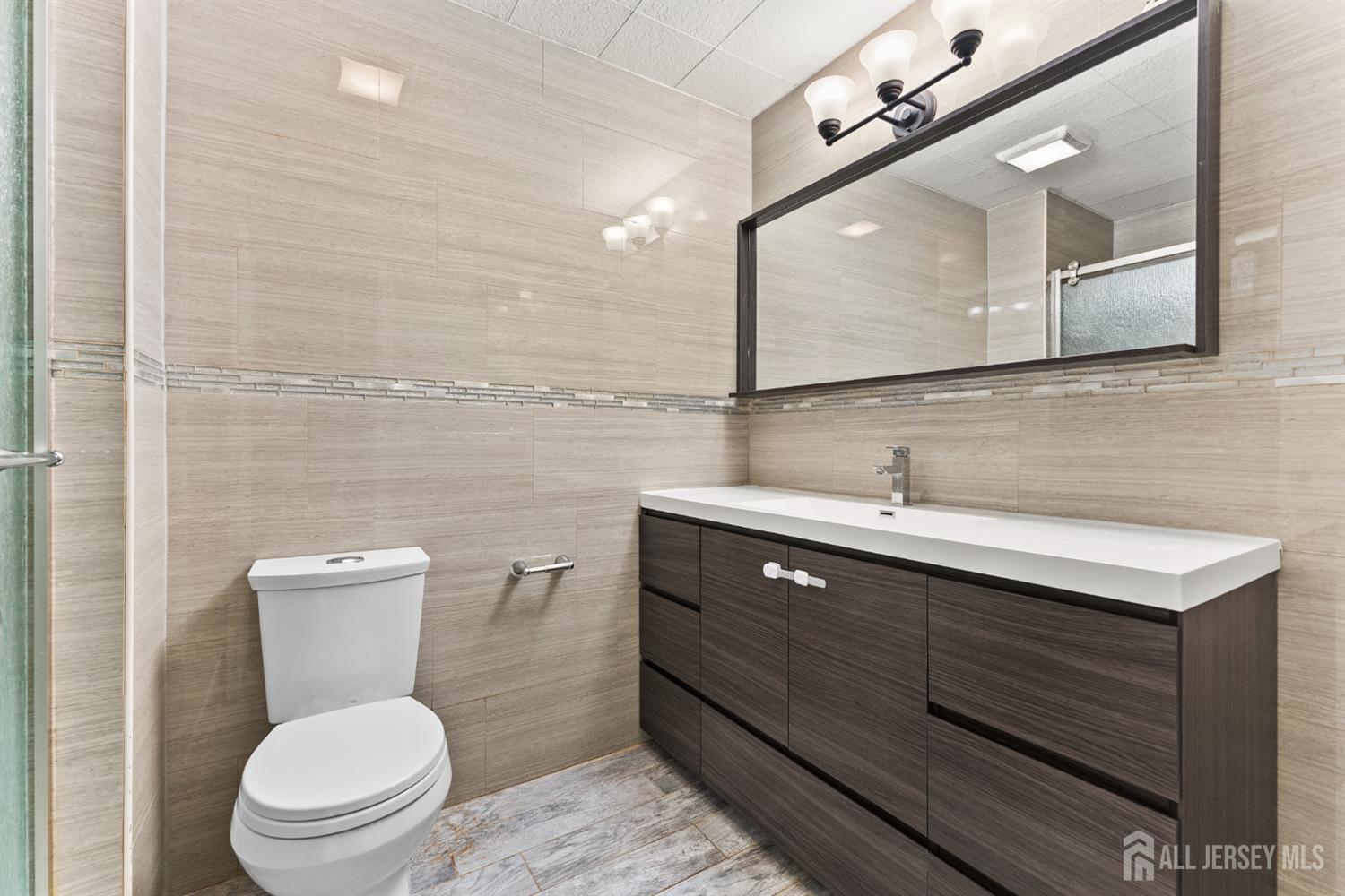 Bathroom with beige tiled walls, dark wood vanity, large mirror, and white toilet.
