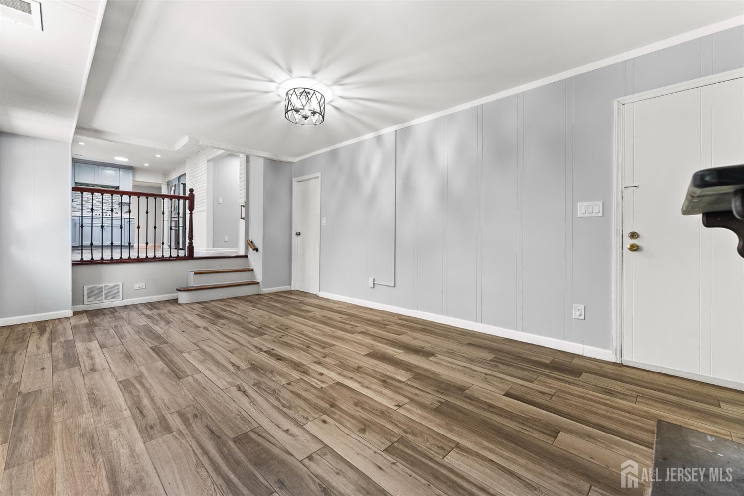 Empty room with wood-look plank flooring, gray paneled walls, and steps leading toward the kitchen.