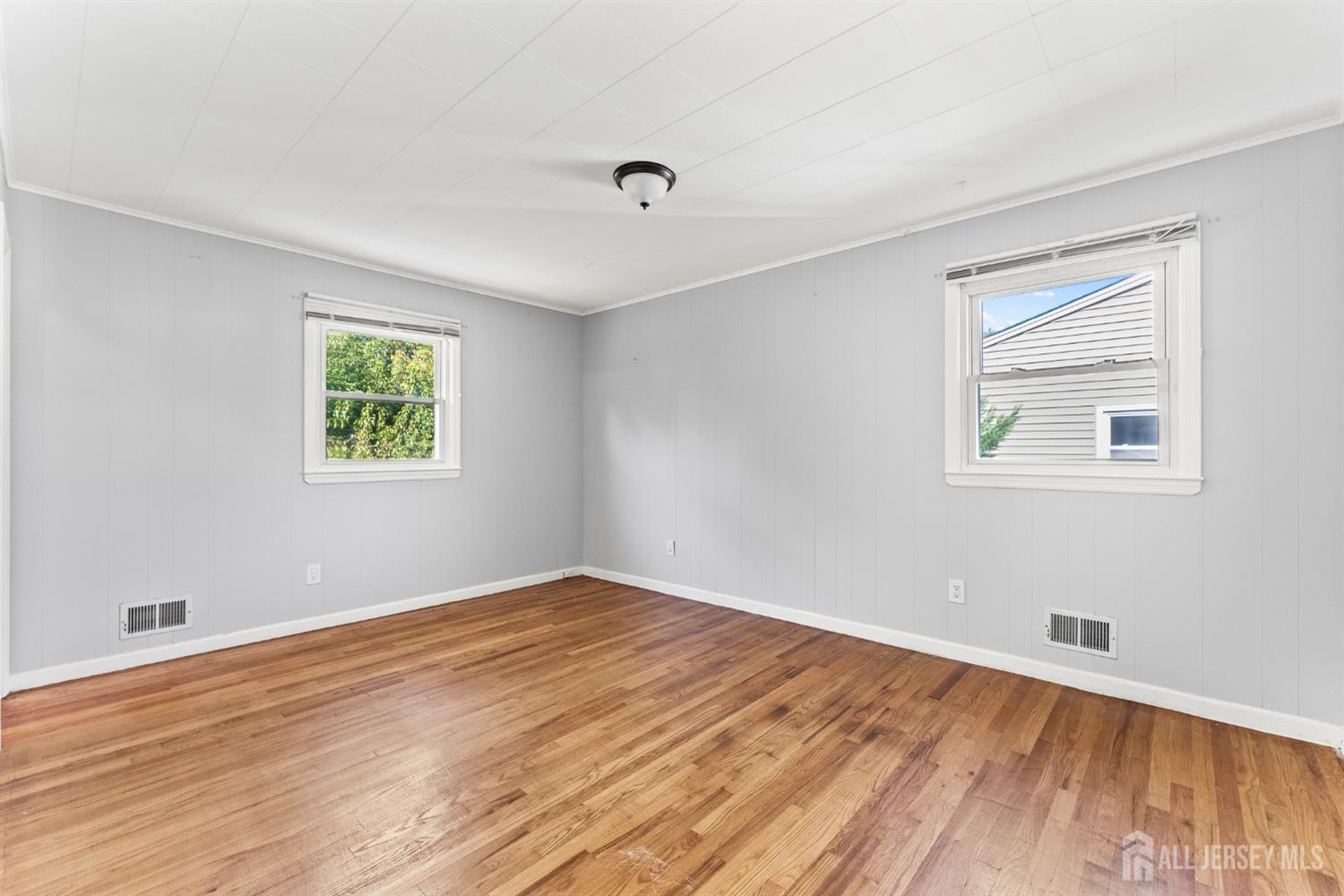 Empty room with hardwood floors, gray walls, and two windows.