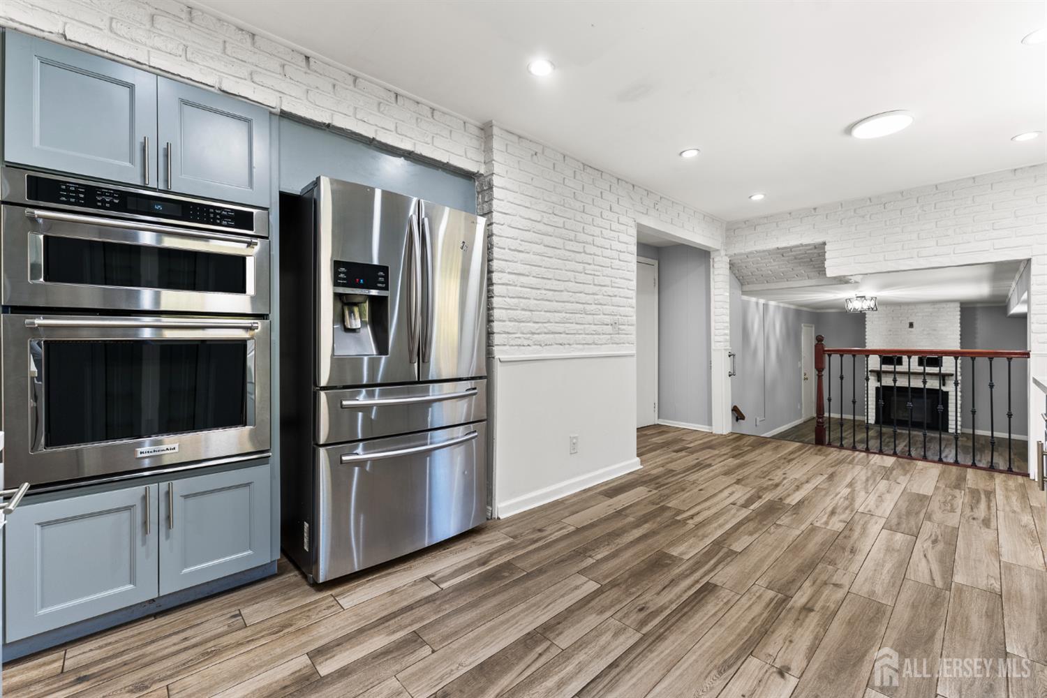 Kitchen with blue-gray cabinets, stainless steel appliances, white brick walls, and wood-look tile flooring.