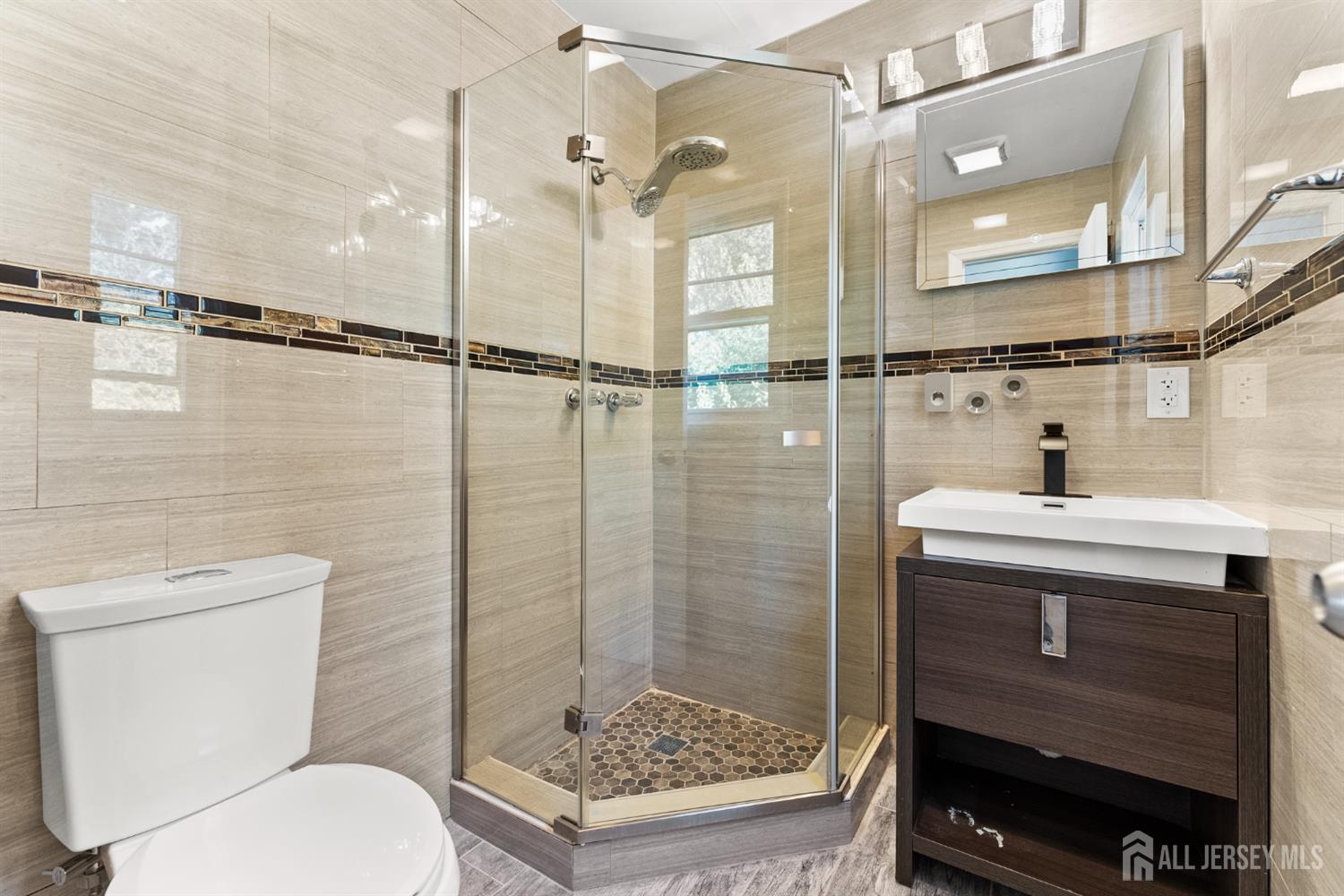Bathroom with a glass corner shower, mosaic floor, dark wood vanity, and beige tile.