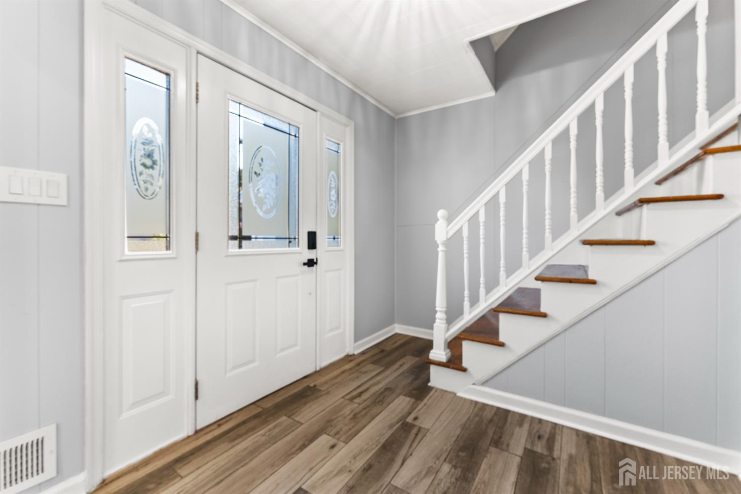 Entry foyer with a glass-paneled front door, wood-look flooring, and a staircase with white railing.