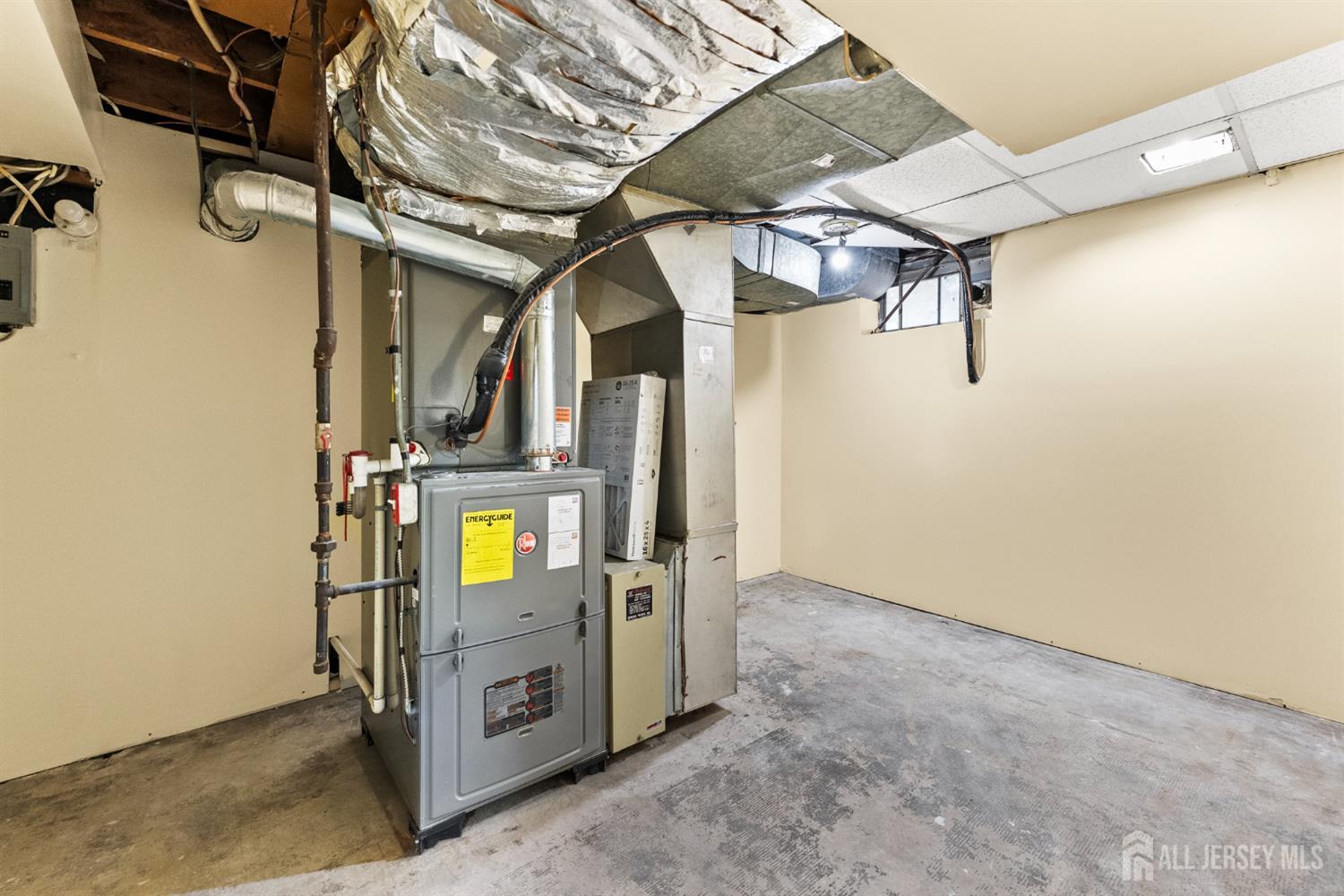 Basement utility room with a large furnace, exposed ductwork, and a bare concrete floor.