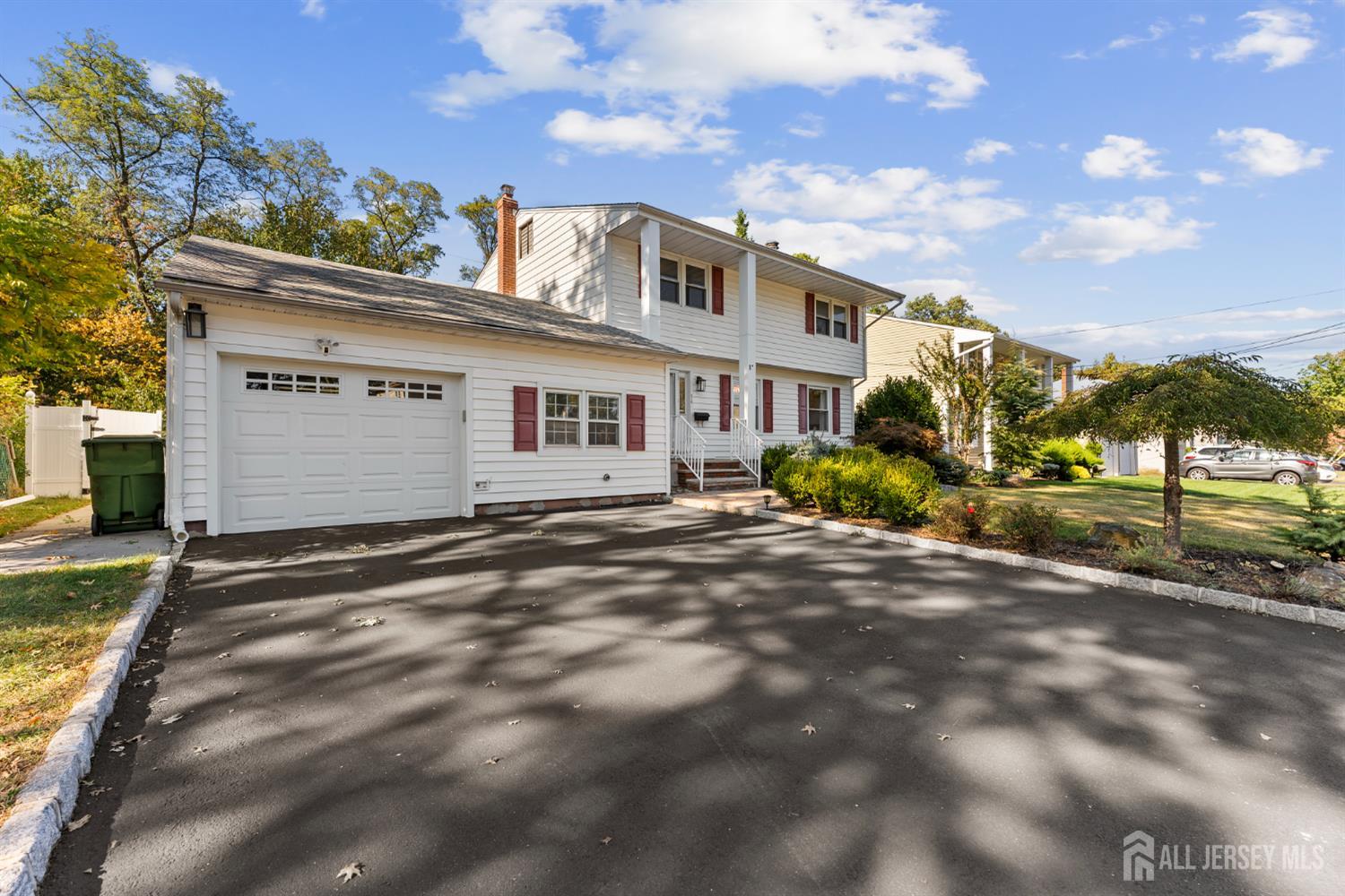 White two-story house with red shutters, attached garage, and broad paved driveway.