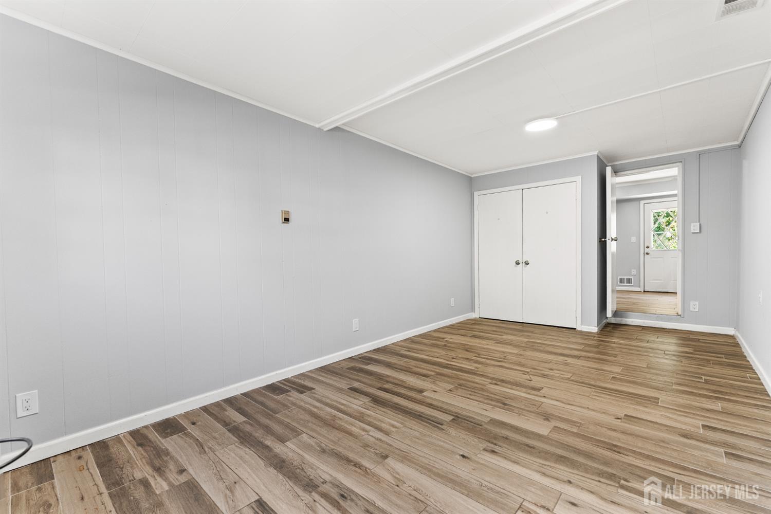 Empty room with gray paneled walls, wood-look plank flooring, and a double-door closet.