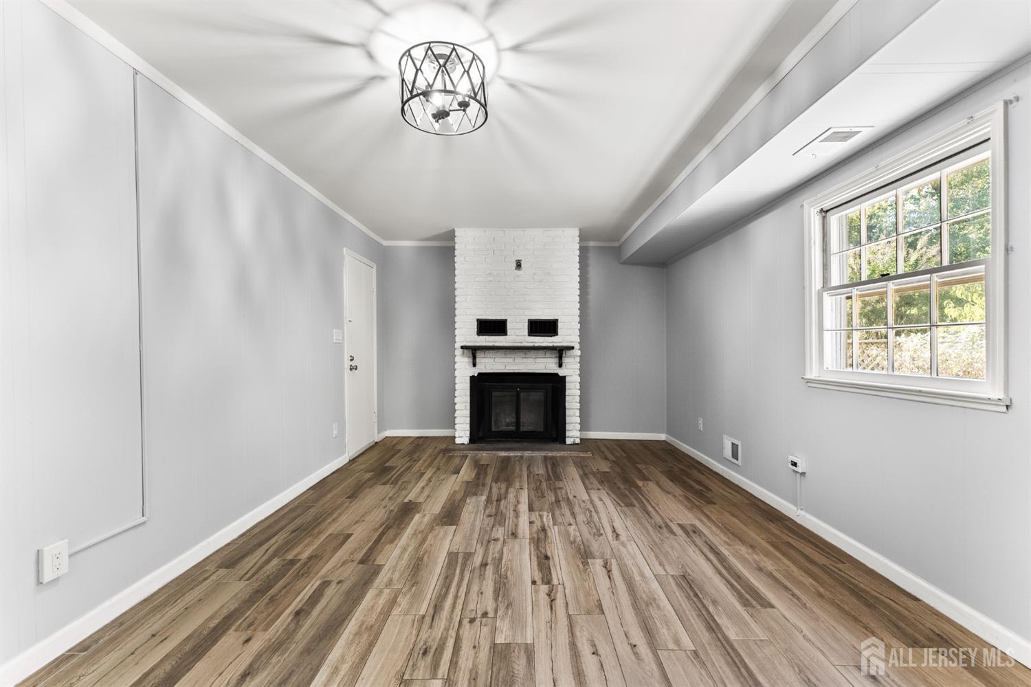 Empty living room with vaulted ceiling, wood-look flooring, and white brick fireplace.