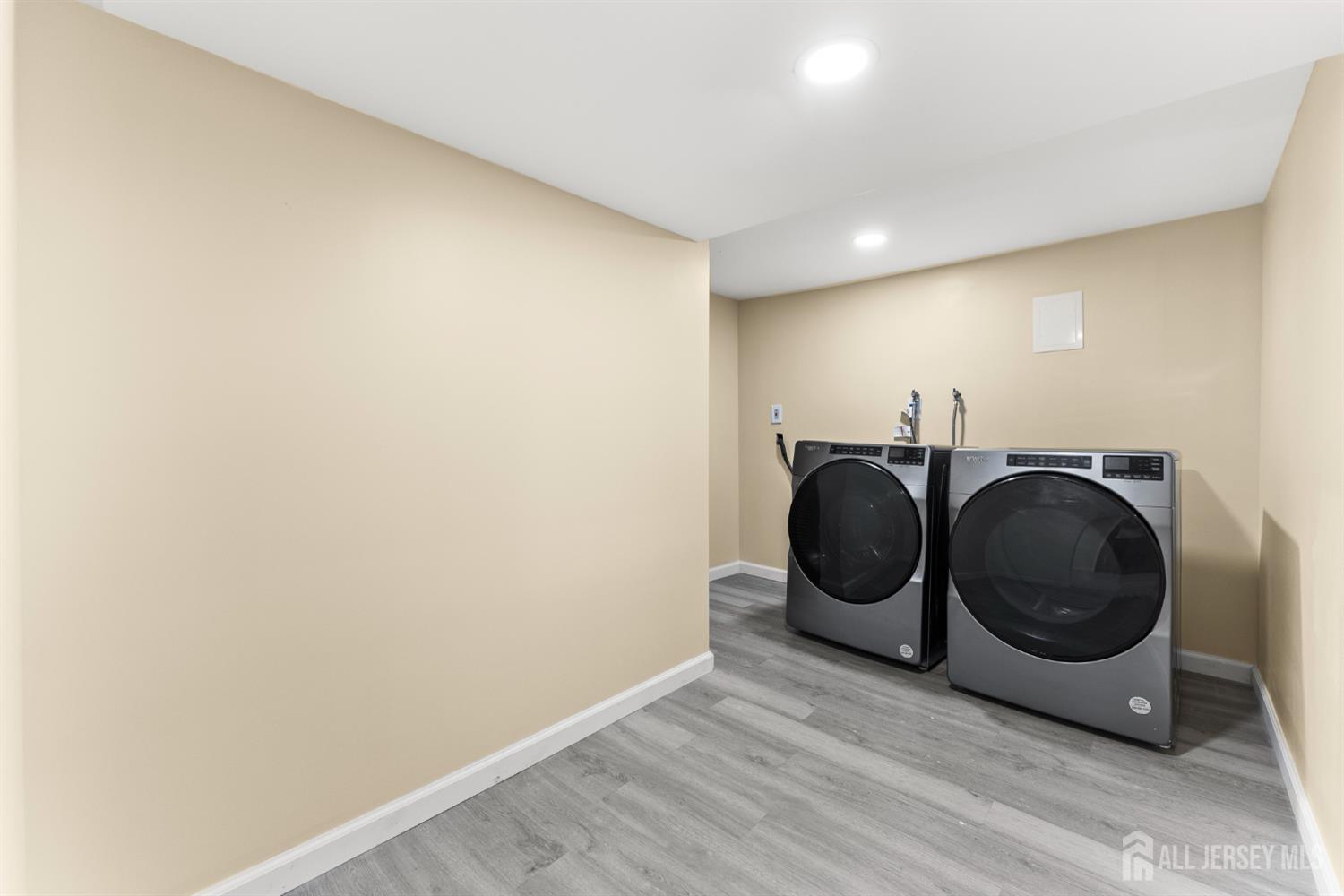 Laundry room with side-by-side front-loading washer and dryer on gray wood-look flooring.