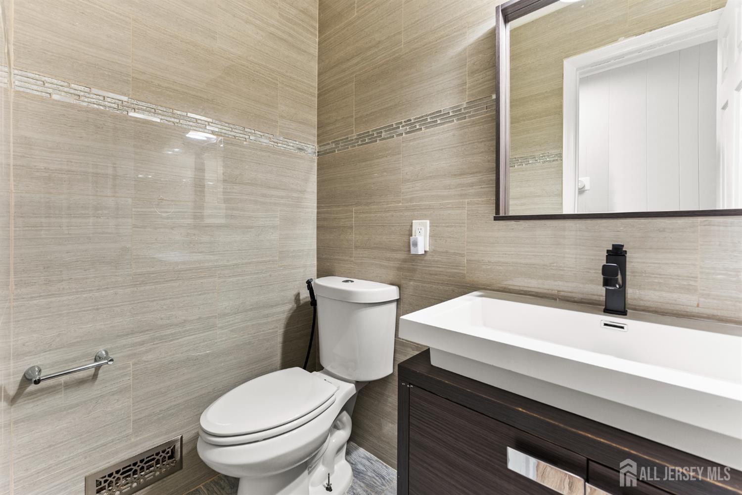 Bathroom with beige tile, a white tub and toilet, and a dark wood vanity.