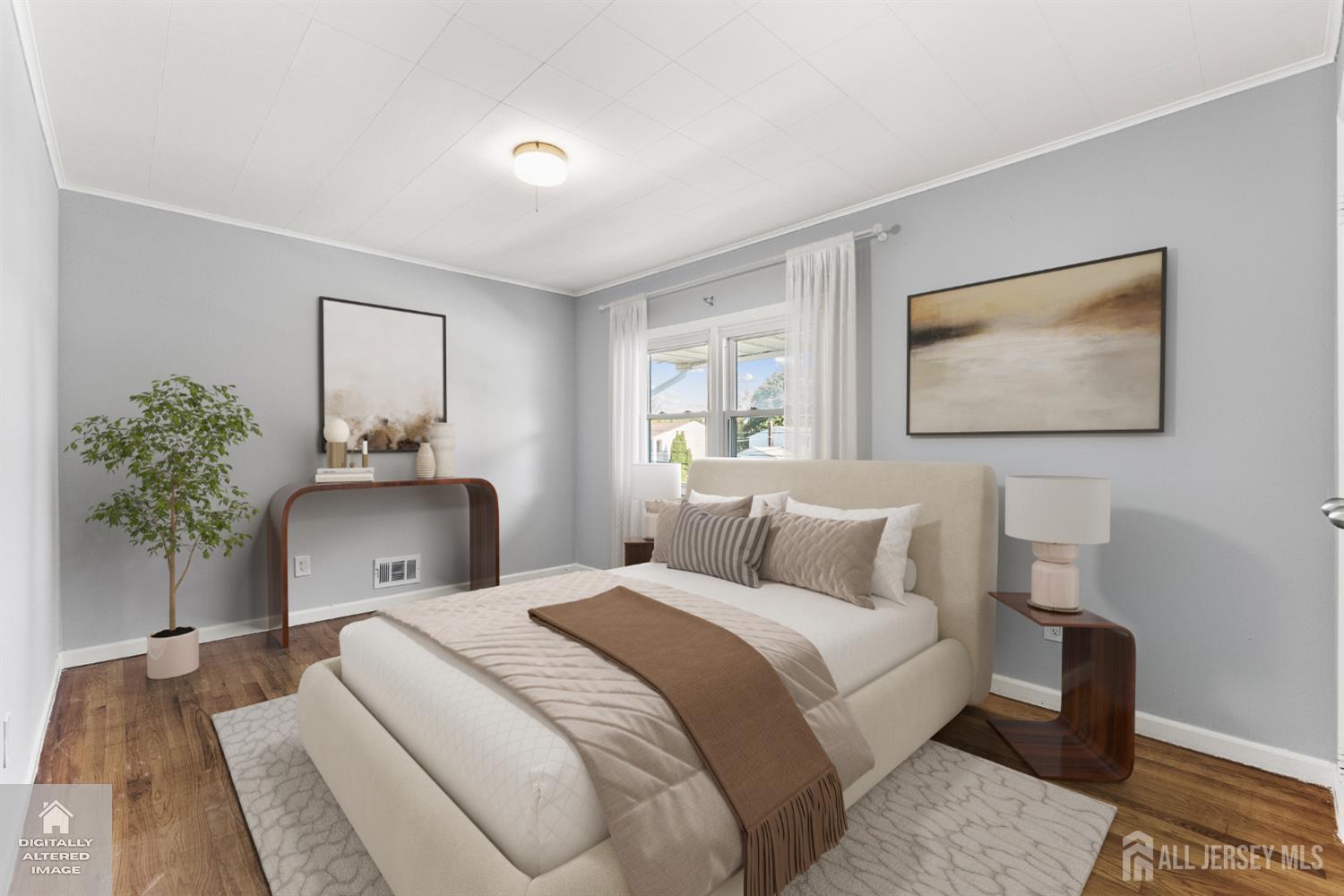 Staged bedroom with a cream bed, neutral bedding, gray walls, and wood floors.