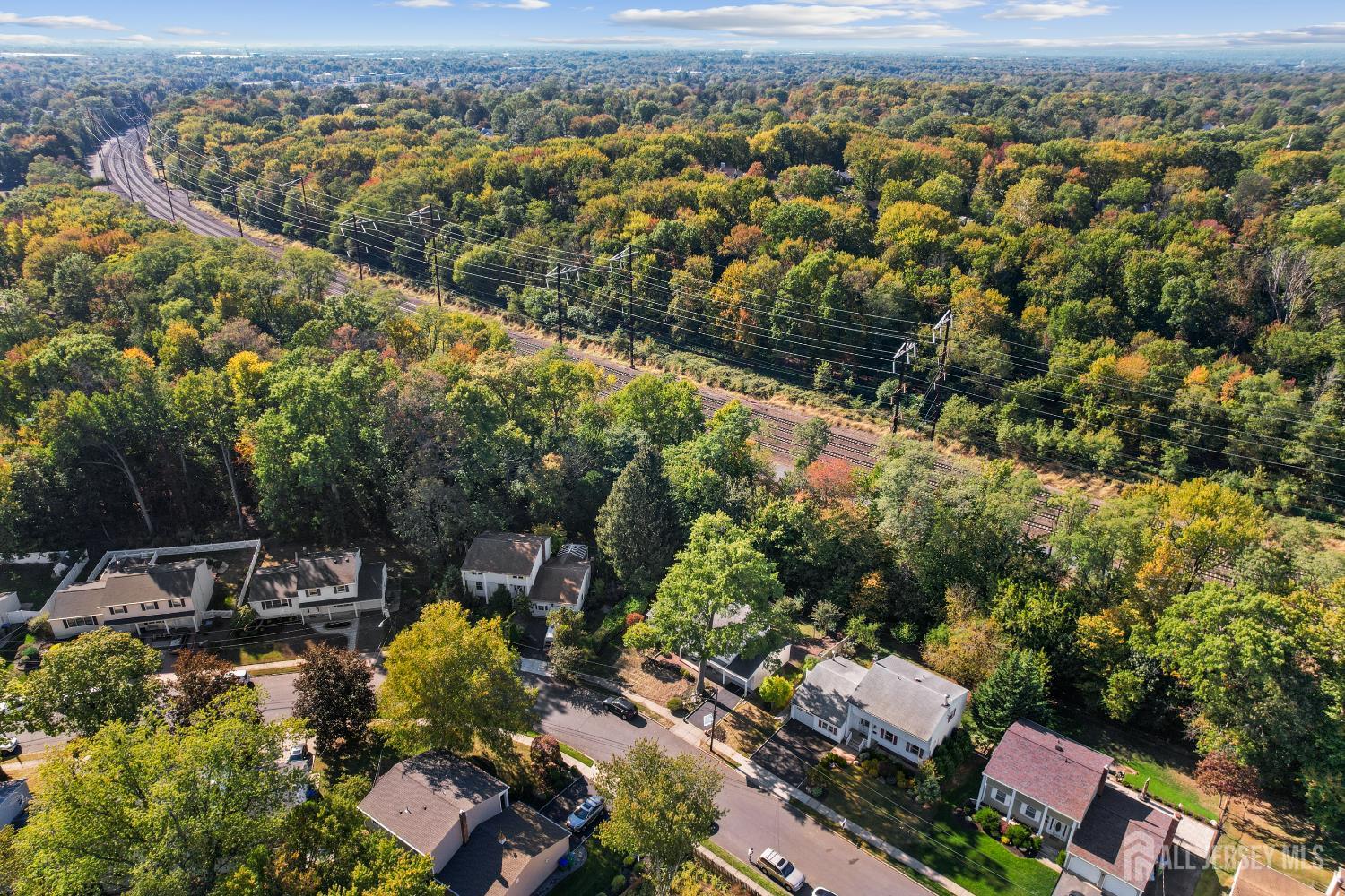 Aerial neighborhood view with autumn woods and railroad tracks behind the homes.