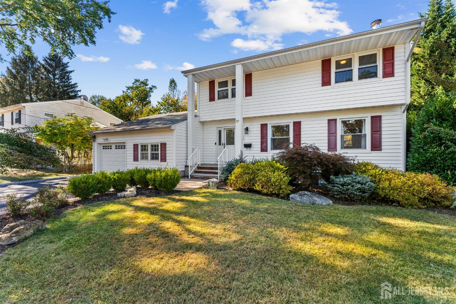 White two-story house with red shutters, attached garage, and landscaped front lawn.