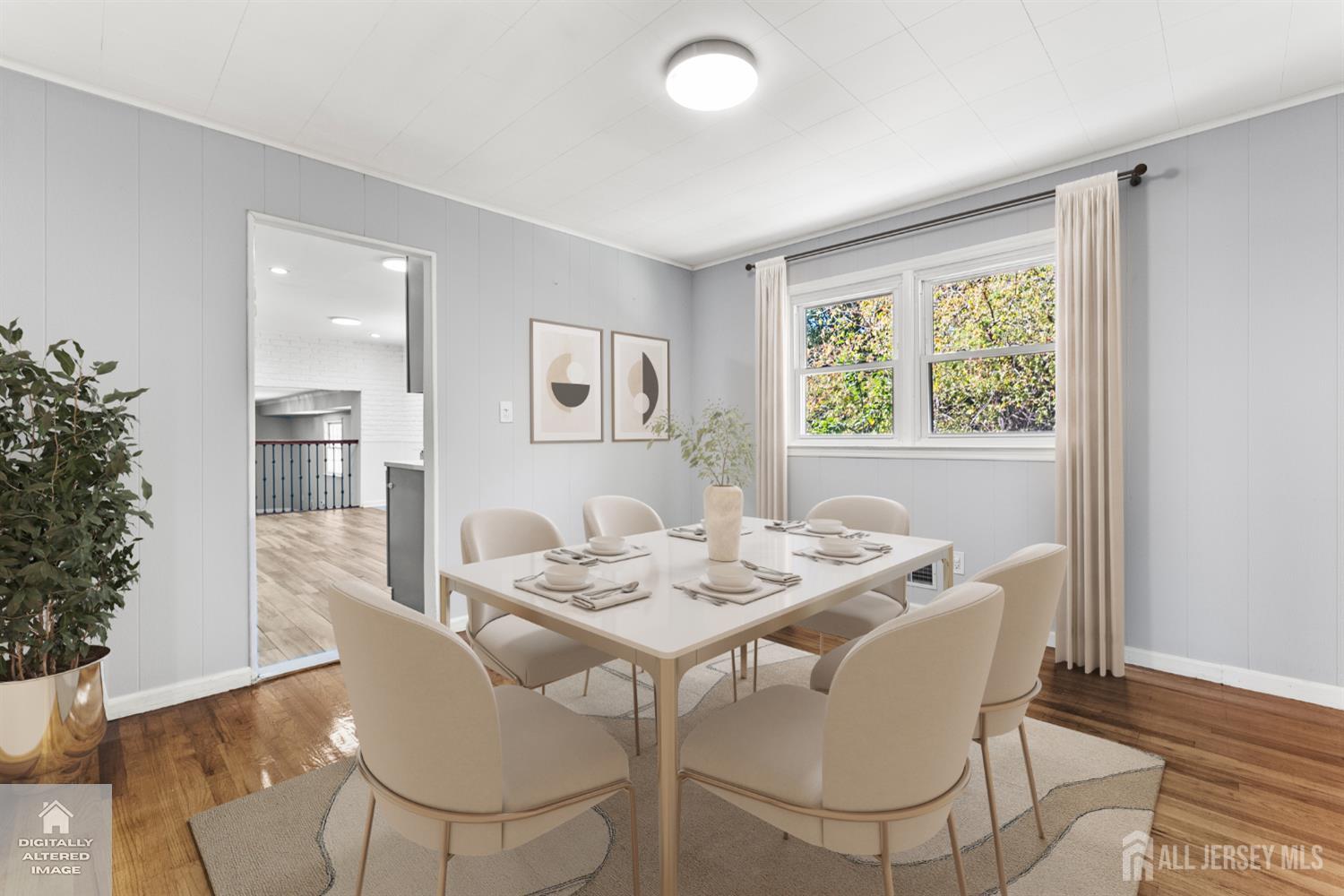 Staged dining room with a set table, cream chairs, hardwood floors, and a large curtained window.