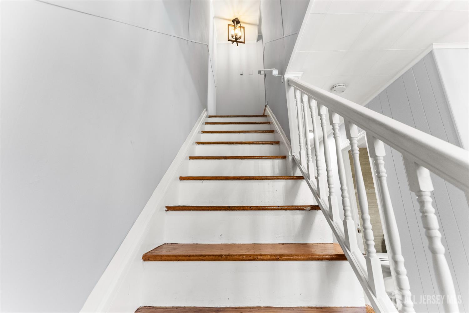 White staircase with brown wooden treads, a turned-baluster railing, and a hanging lantern.