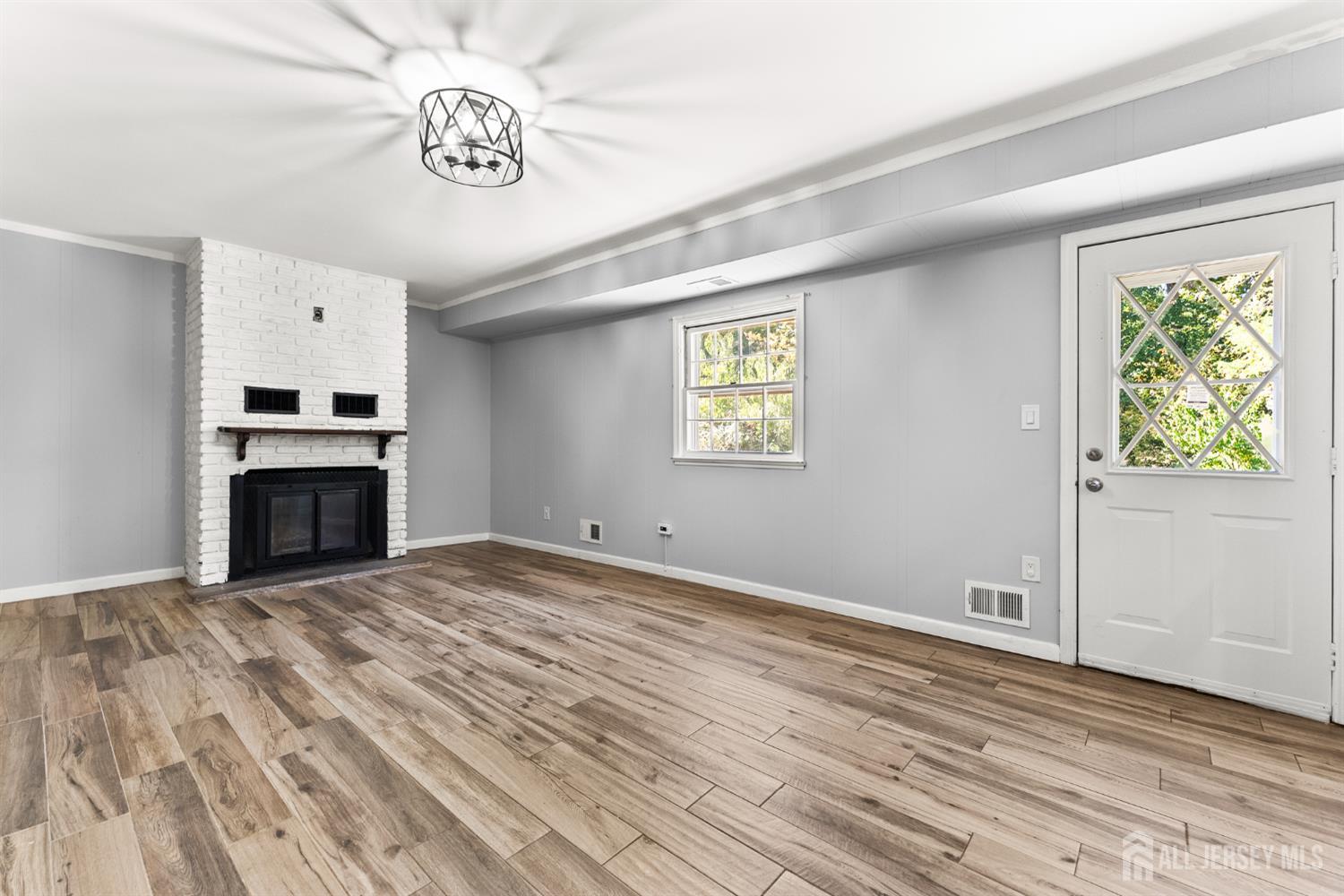 Empty living room with a white brick fireplace, wood-look flooring, and a diamond-pane glass door.